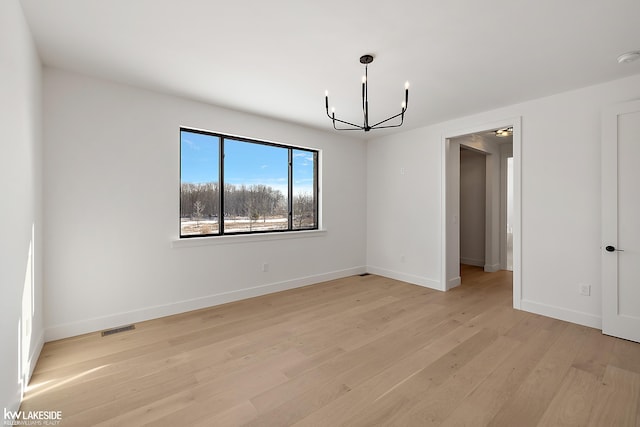 empty room featuring light hardwood / wood-style floors and a notable chandelier