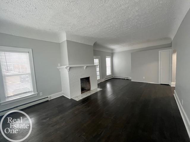 unfurnished living room featuring dark hardwood / wood-style floors, a fireplace, baseboard heating, and a textured ceiling