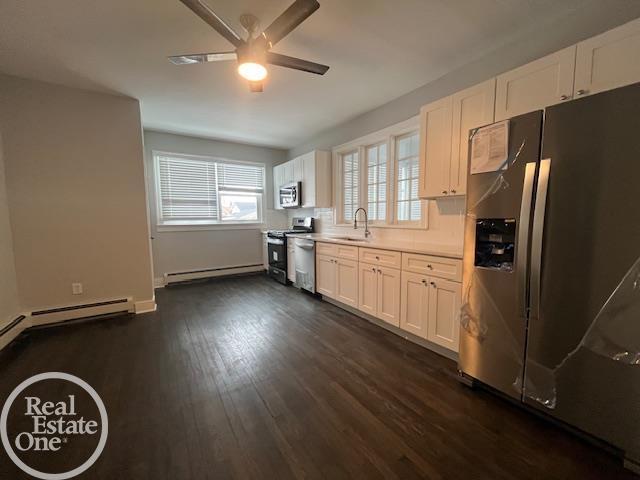 kitchen featuring white cabinetry, a baseboard radiator, dark hardwood / wood-style flooring, ceiling fan, and stainless steel appliances