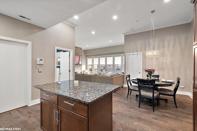 kitchen featuring ornamental molding, dark stone countertops, a center island, and dark hardwood / wood-style flooring