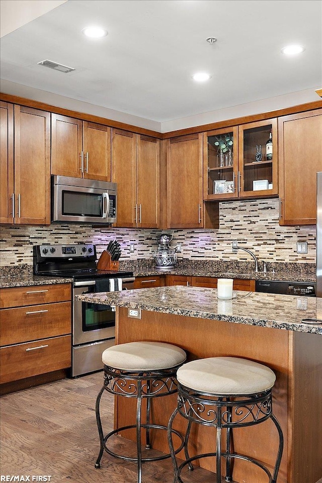 kitchen featuring dark stone counters, appliances with stainless steel finishes, a breakfast bar, and light hardwood / wood-style flooring