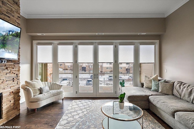 living room featuring dark hardwood / wood-style flooring, crown molding, and a stone fireplace