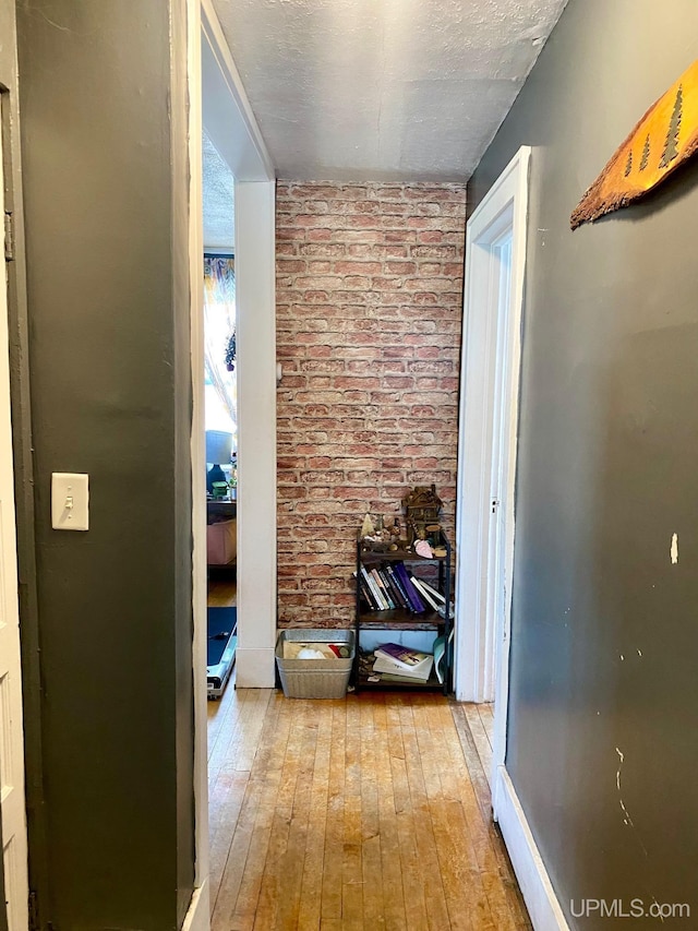 hallway with brick wall, light hardwood / wood-style floors, and a textured ceiling