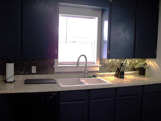 kitchen with light stone countertops, black dishwasher, sink, and decorative backsplash