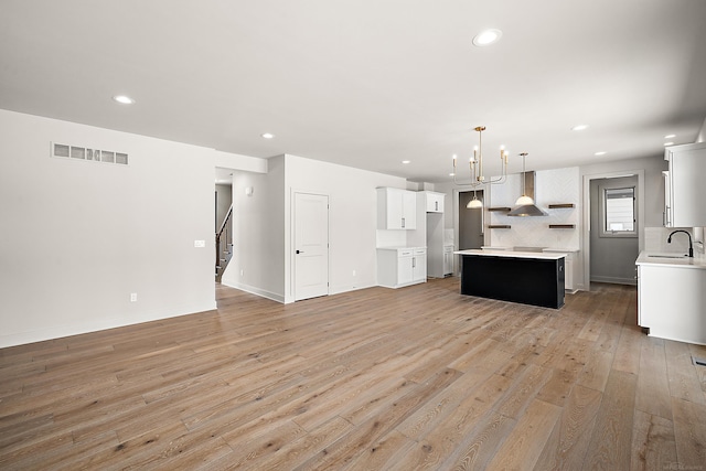 kitchen featuring pendant lighting, sink, white cabinetry, a center island, and light wood-type flooring