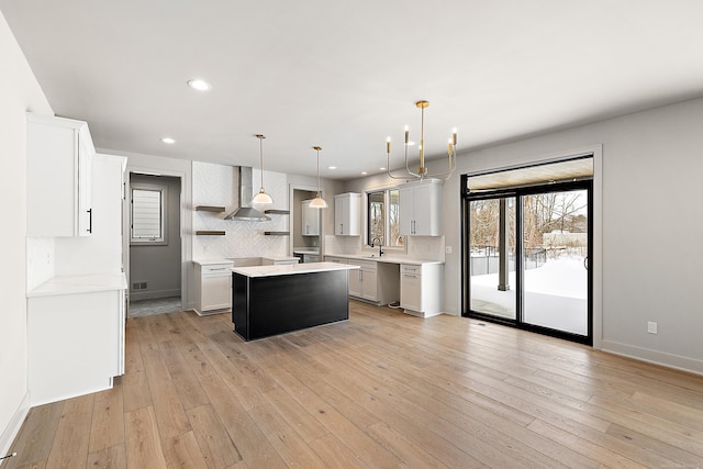 kitchen featuring wall chimney range hood, hanging light fixtures, a center island, white cabinets, and light wood-type flooring