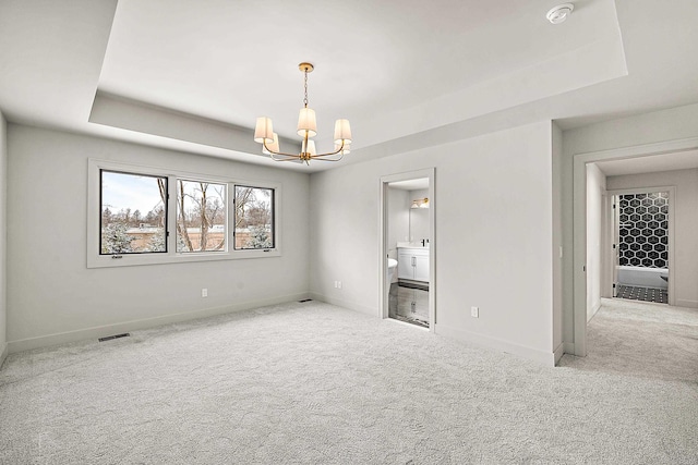 spare room with an inviting chandelier, a raised ceiling, and light carpet