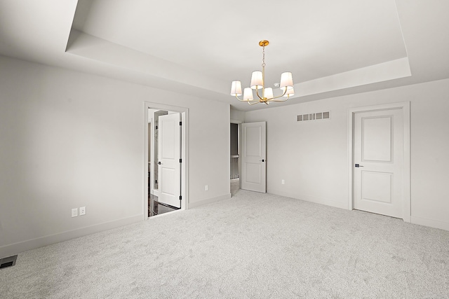 unfurnished room featuring a chandelier, a raised ceiling, and carpet floors