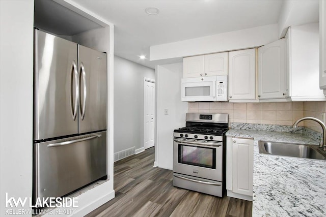 kitchen with appliances with stainless steel finishes, tasteful backsplash, sink, white cabinets, and light stone countertops