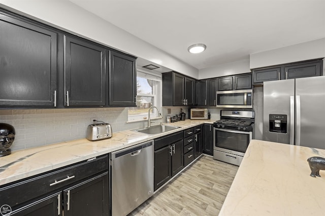 kitchen with sink, light stone counters, light wood-type flooring, stainless steel appliances, and backsplash