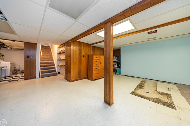 basement with a paneled ceiling and wood walls