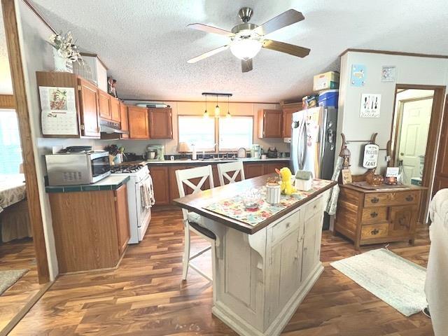 kitchen with stainless steel microwave, gas range gas stove, under cabinet range hood, freestanding refrigerator, and wood finished floors