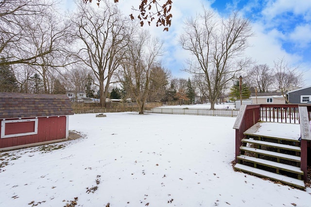 yard covered in snow with a wooden deck and a storage unit