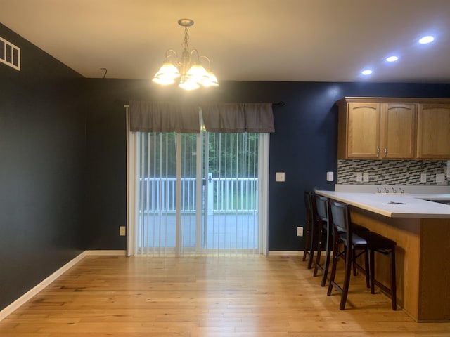 kitchen with an inviting chandelier, decorative backsplash, hanging light fixtures, and light hardwood / wood-style flooring