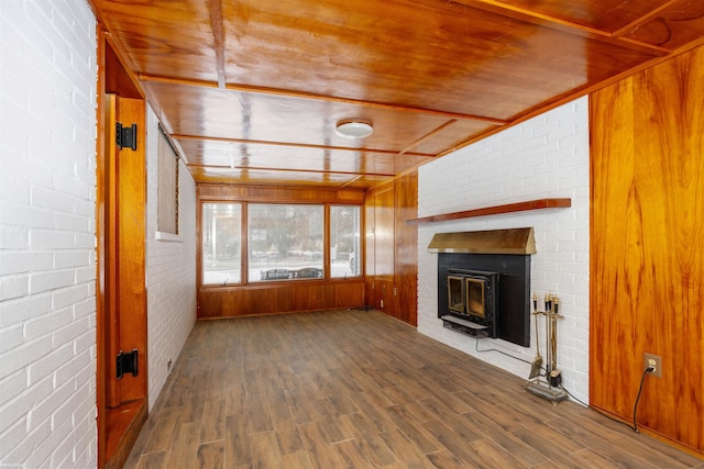 unfurnished living room featuring dark hardwood / wood-style flooring, a brick fireplace, wooden walls, and brick wall