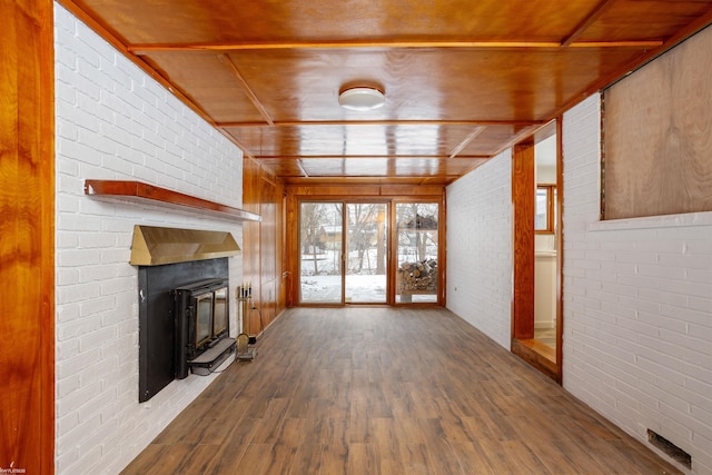 unfurnished living room featuring hardwood / wood-style flooring, a large fireplace, and brick wall