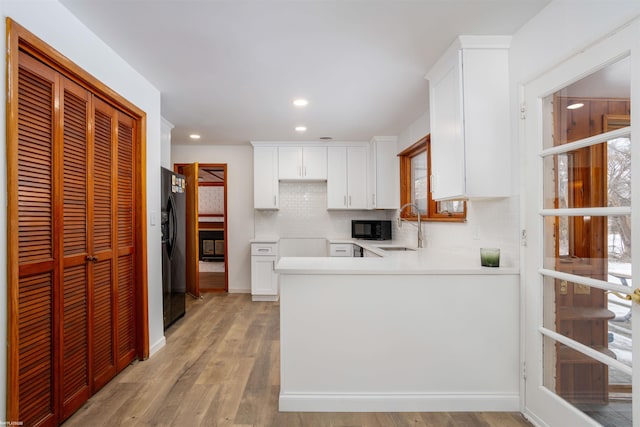 kitchen featuring sink, light hardwood / wood-style flooring, tasteful backsplash, black appliances, and white cabinets