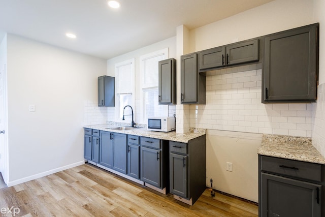 kitchen with sink, light stone counters, backsplash, and light wood-type flooring