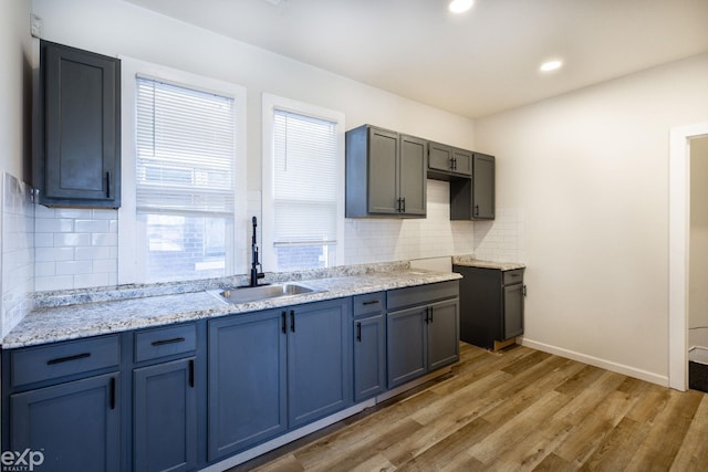 kitchen with light stone counters, sink, backsplash, and hardwood / wood-style floors