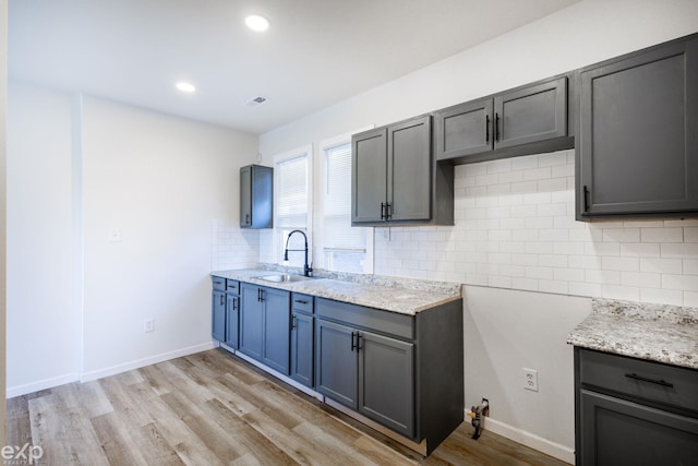 kitchen featuring sink, light stone counters, light hardwood / wood-style flooring, gray cabinets, and backsplash