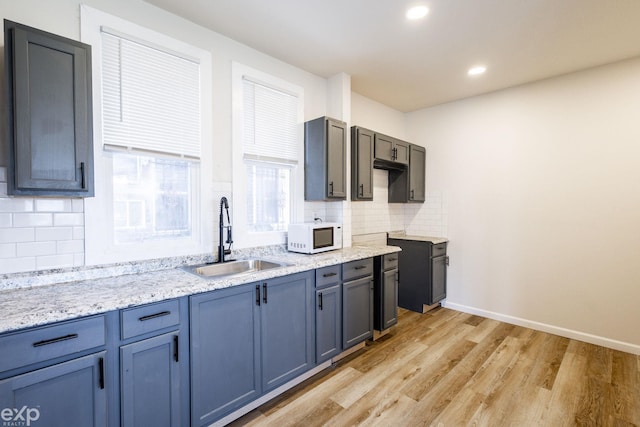 kitchen featuring sink, decorative backsplash, light stone countertops, and light wood-type flooring