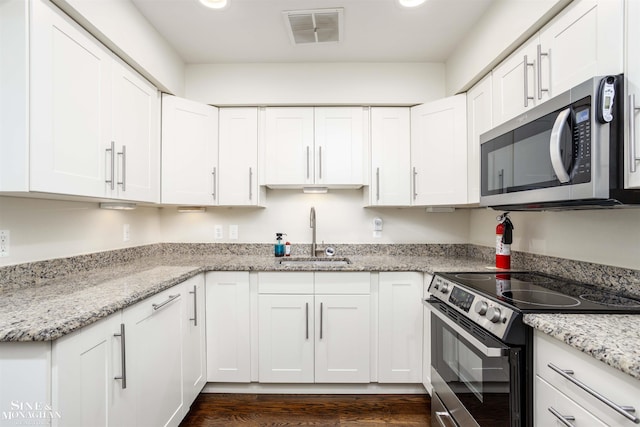 kitchen with appliances with stainless steel finishes, sink, white cabinets, light stone counters, and dark wood-type flooring