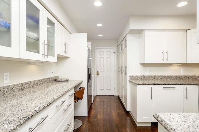 kitchen with light stone countertops, dark wood-type flooring, high end refrigerator, and white cabinets