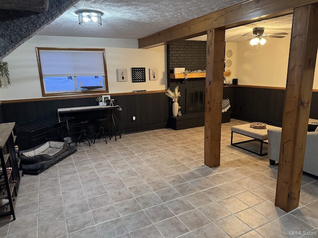 basement with wood walls, light tile patterned floors, ceiling fan, a brick fireplace, and a textured ceiling