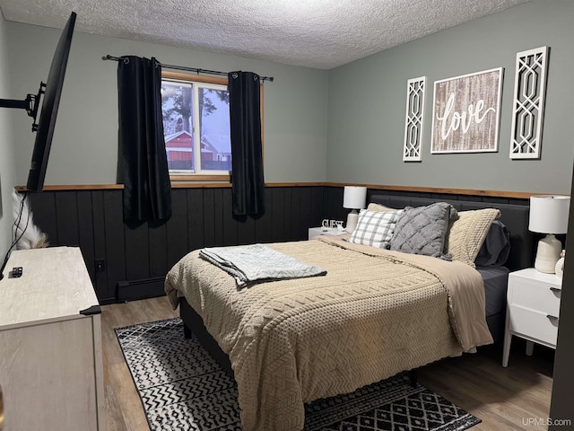 bedroom featuring baseboard heating, light hardwood / wood-style floors, and a textured ceiling