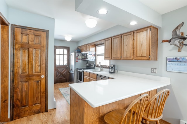 kitchen featuring kitchen peninsula, stainless steel appliances, a breakfast bar, light hardwood / wood-style flooring, and sink