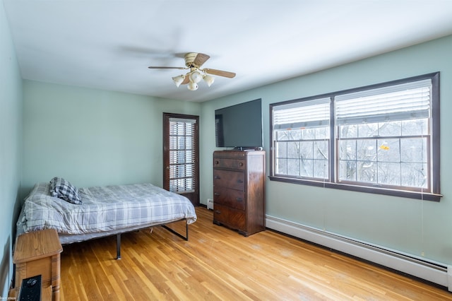 bedroom featuring a baseboard heating unit, ceiling fan, multiple windows, and light hardwood / wood-style floors