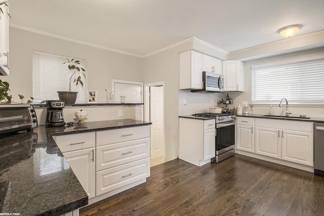 kitchen with sink, ornamental molding, dark stone counters, appliances with stainless steel finishes, and white cabinets