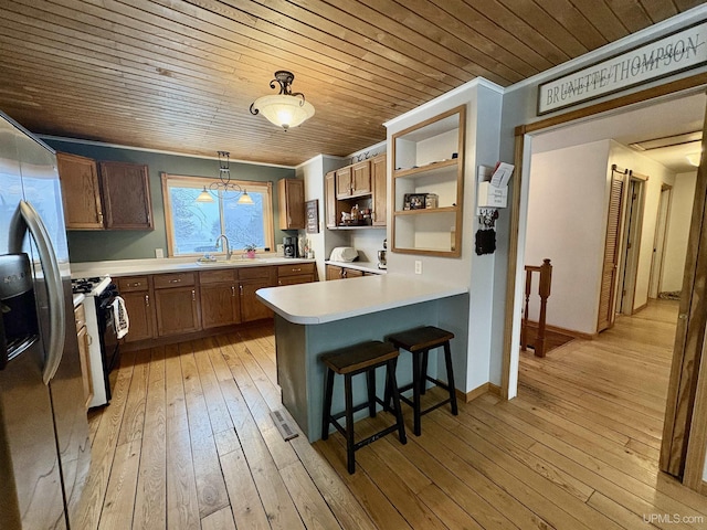 kitchen with light wood-type flooring, stainless steel fridge with ice dispenser, gas range oven, kitchen peninsula, and hanging light fixtures