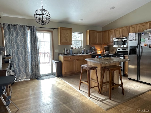 kitchen with appliances with stainless steel finishes, vaulted ceiling, a kitchen bar, a center island, and pendant lighting