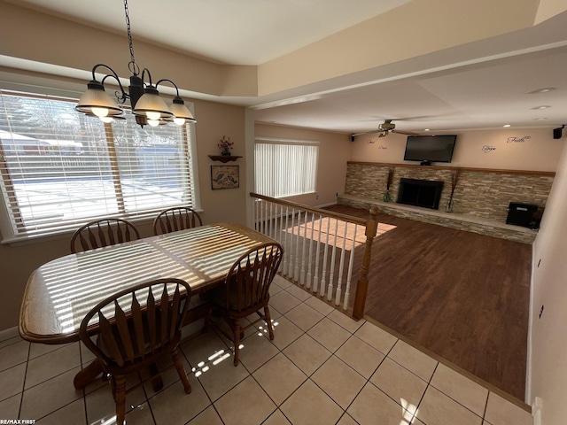 dining space with ceiling fan with notable chandelier, light tile patterned floors, and a fireplace