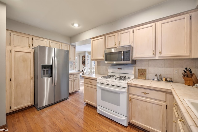 kitchen featuring tile counters, decorative backsplash, stainless steel appliances, and light hardwood / wood-style floors