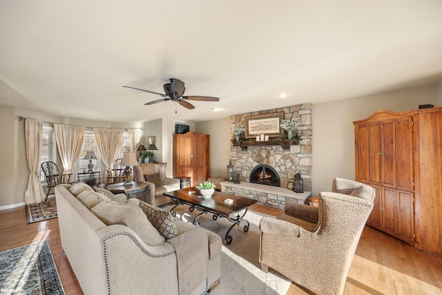 living room with light wood-type flooring, ceiling fan, and a stone fireplace