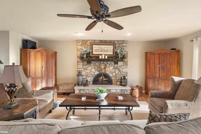 living room with light wood-type flooring, ceiling fan, and a stone fireplace