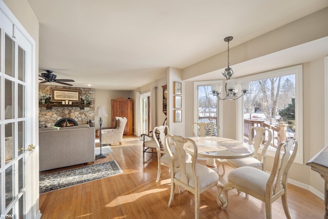 dining space with ceiling fan with notable chandelier, light wood-type flooring, and a stone fireplace