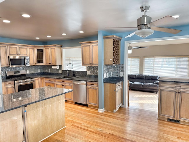 kitchen featuring tasteful backsplash, stainless steel appliances, light hardwood / wood-style floors, sink, and dark stone countertops