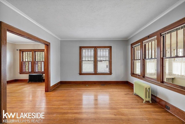 empty room featuring radiator, light hardwood / wood-style flooring, a textured ceiling, and ornamental molding