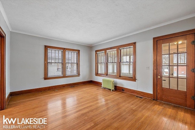 empty room with light wood-type flooring, ornamental molding, radiator heating unit, and plenty of natural light