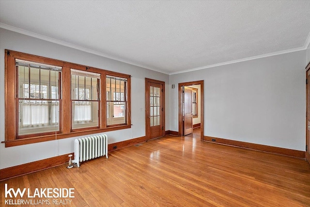 empty room featuring a textured ceiling, radiator, light hardwood / wood-style floors, and a wealth of natural light