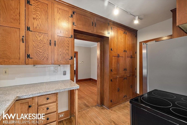 kitchen with light hardwood / wood-style flooring, backsplash, range with electric cooktop, crown molding, and stainless steel fridge