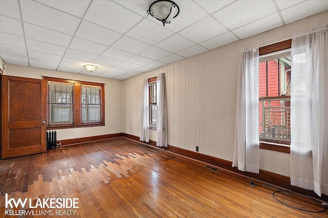 unfurnished room with radiator, a paneled ceiling, a wealth of natural light, and hardwood / wood-style floors