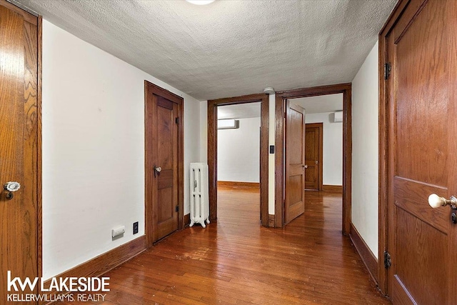 corridor featuring a textured ceiling, hardwood / wood-style flooring, and radiator heating unit