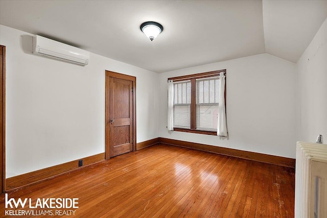 unfurnished room featuring radiator, hardwood / wood-style flooring, lofted ceiling, and a wall mounted air conditioner