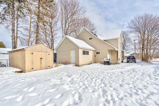 snow covered back of property featuring a storage unit