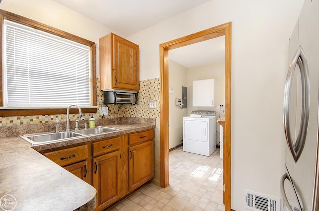 kitchen featuring electric panel, sink, washer / clothes dryer, stainless steel refrigerator, and tasteful backsplash