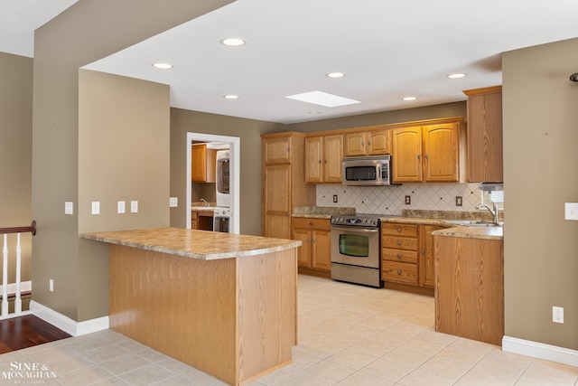 kitchen featuring sink, a skylight, stainless steel appliances, kitchen peninsula, and decorative backsplash